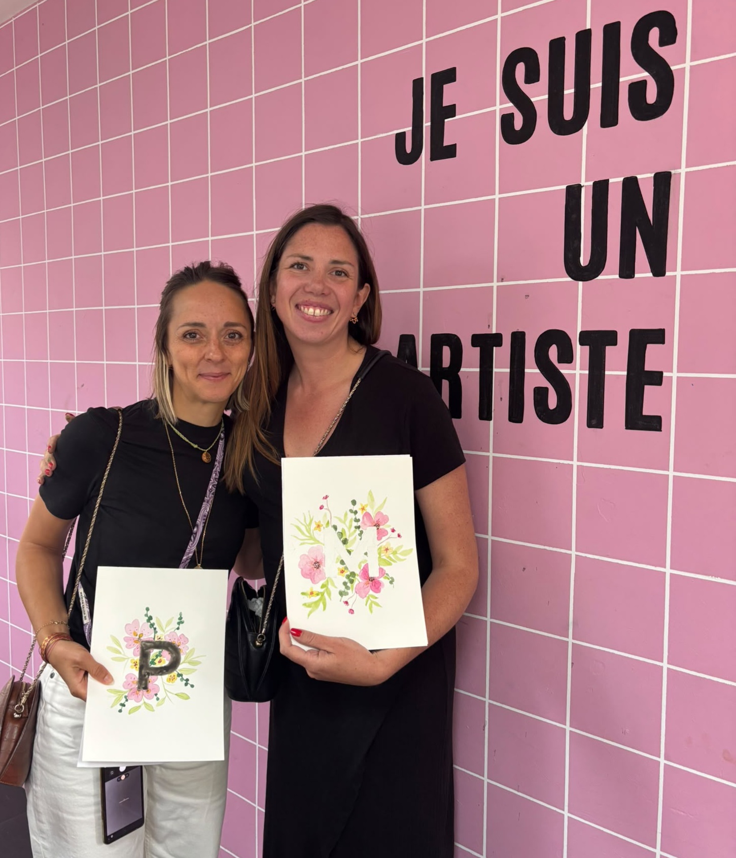 Deux participantes présentent leur aquarelle devant le mur « Je suis un artiste » chez Rartistes